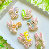 Playful bunnies holding E A S T E R letters stamp and cutter